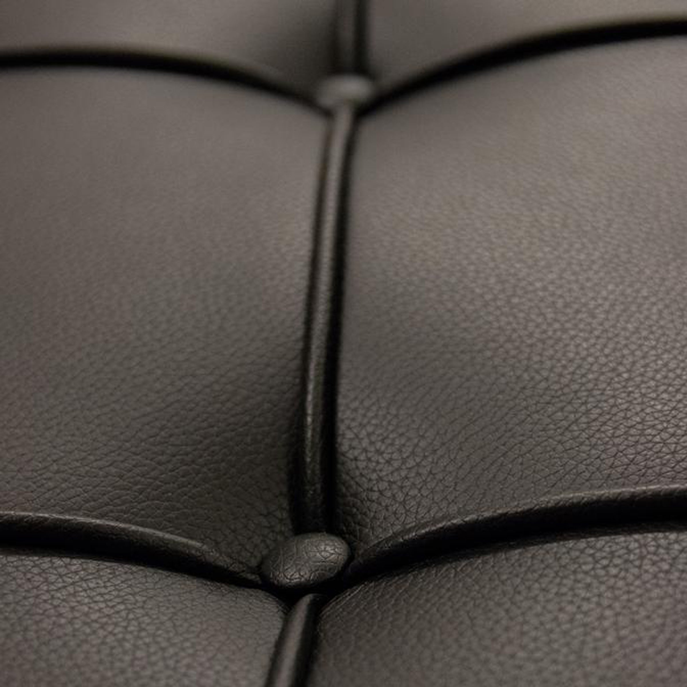 Makroaufnahme des schwarzen Leders mit Steppnähten und Knopfdetails des Barcelona Hockers