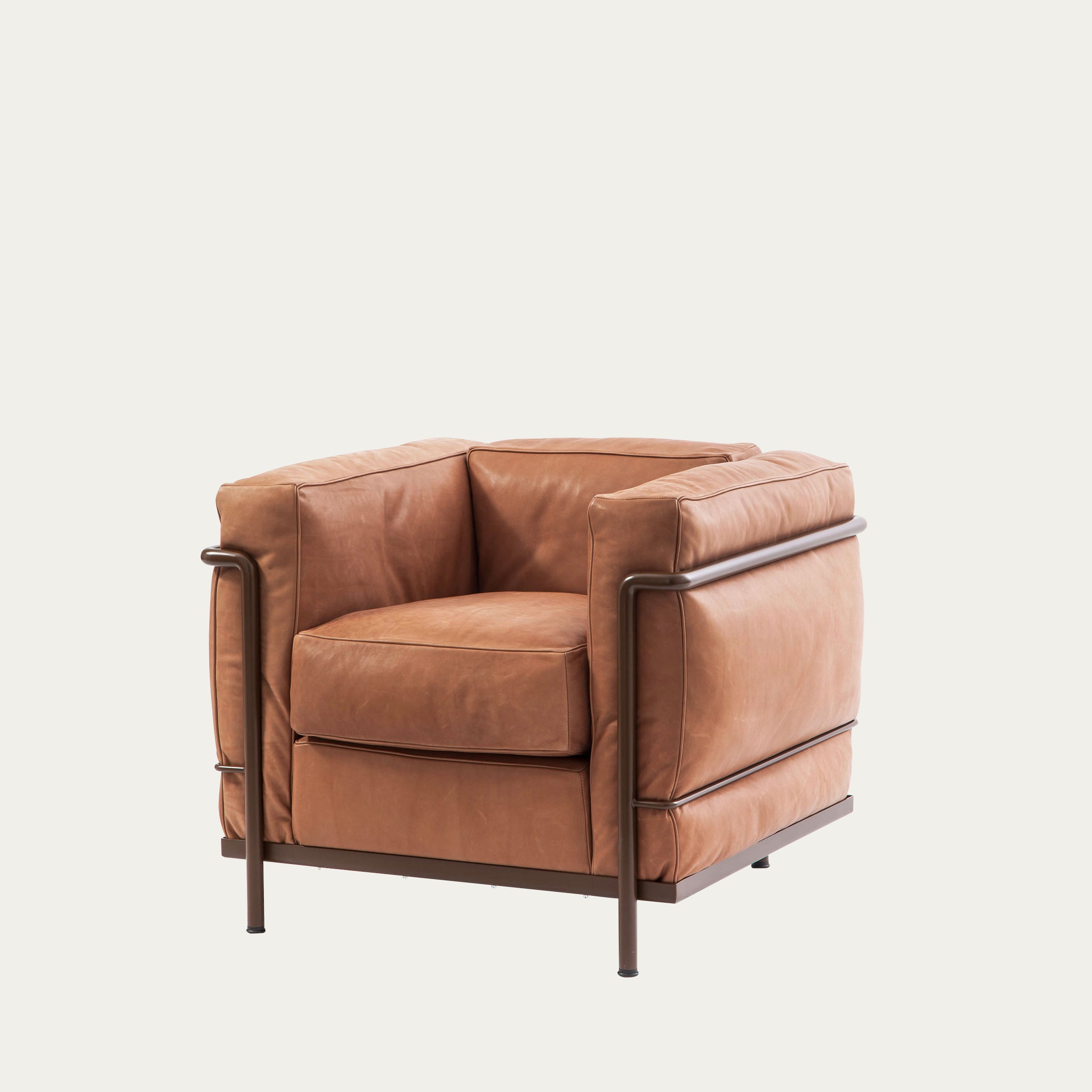 Schrägansicht des LC2 Sessel Petit Modèle von Le Corbusier mit cognacfarbenem Lederbezug und braunem Stahlgestell