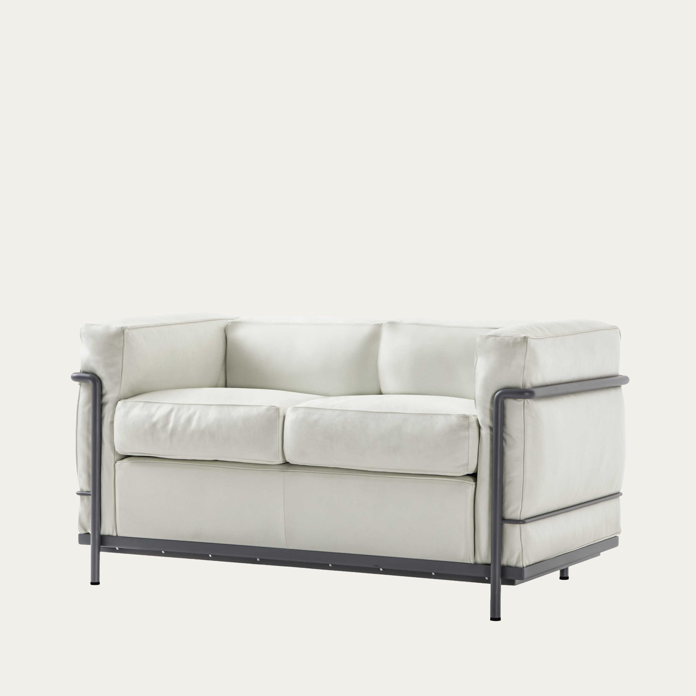 Schrägansicht des LC2 Sofa Petit Modèle – Zweisitzer in cremeweißem Leder mit dunkelgrauem Stahlrahmen